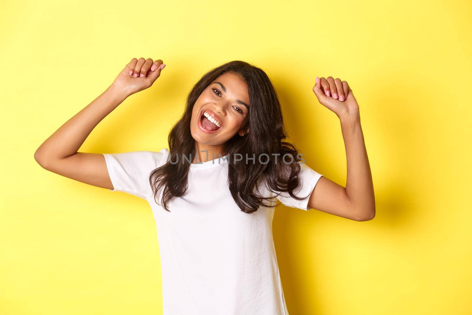 Image of cheerful african-american girl winning, looking happy and celebrating victory, triumphing about achievement, standing over yellow background.