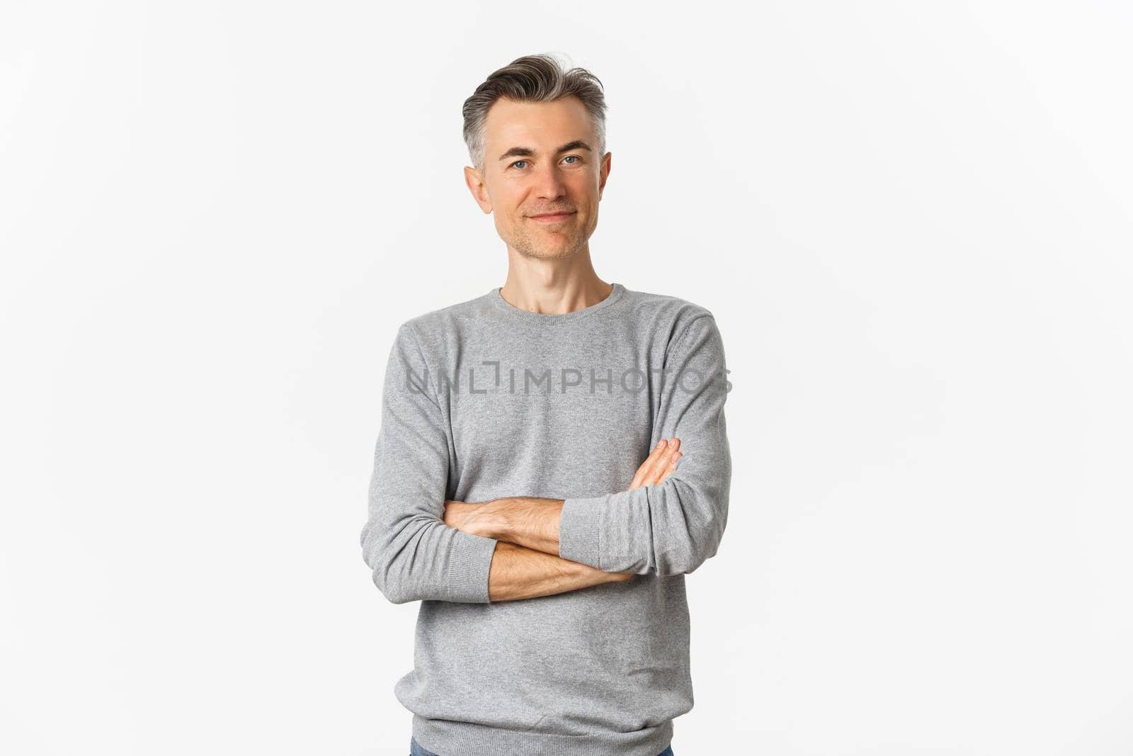 Portrait of attractive middle-aged man standing confident with hands crossed on chest, smiling pleased, posing over white background.