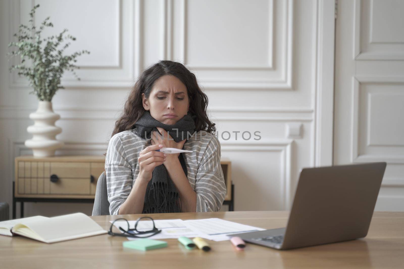 Sick young hispanic woman office worker sitting at workplace holding thermometer by vkstock