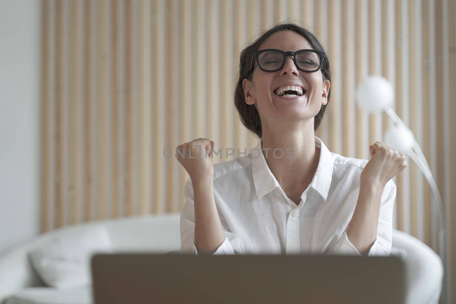 Excited latina woman freelancer clenched her fists with joy and delight with head raised up as if shouting hurray, celebrates joy of finished difficult business project. Remote work concept