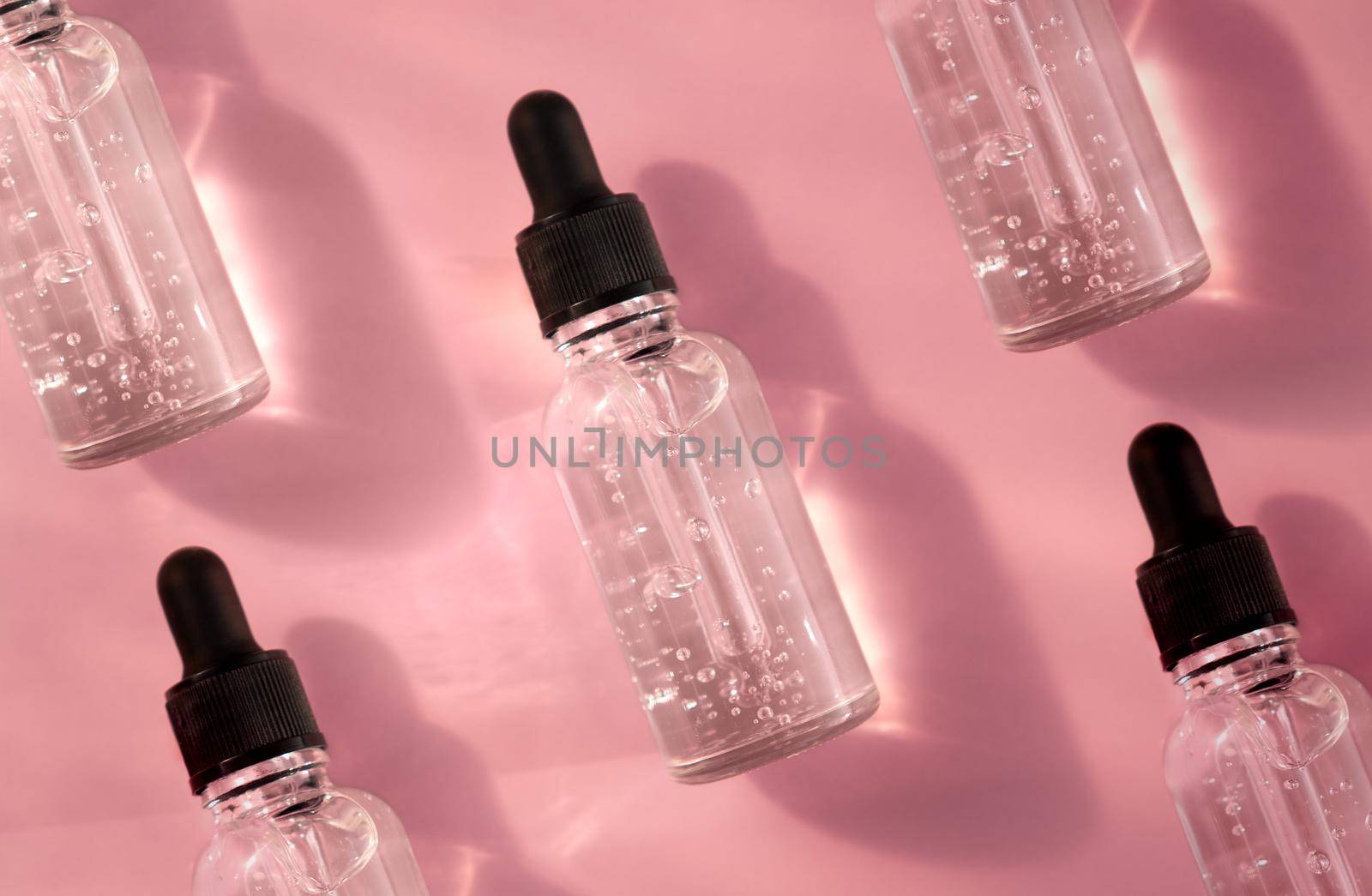 Transparent glass dropper bottle with air bubbles pattern on pink background in sunlight. Pipette with fluid hyaluronic acid, serum, retinol. Cosmetics and healthcare concept. Luxury beauty product