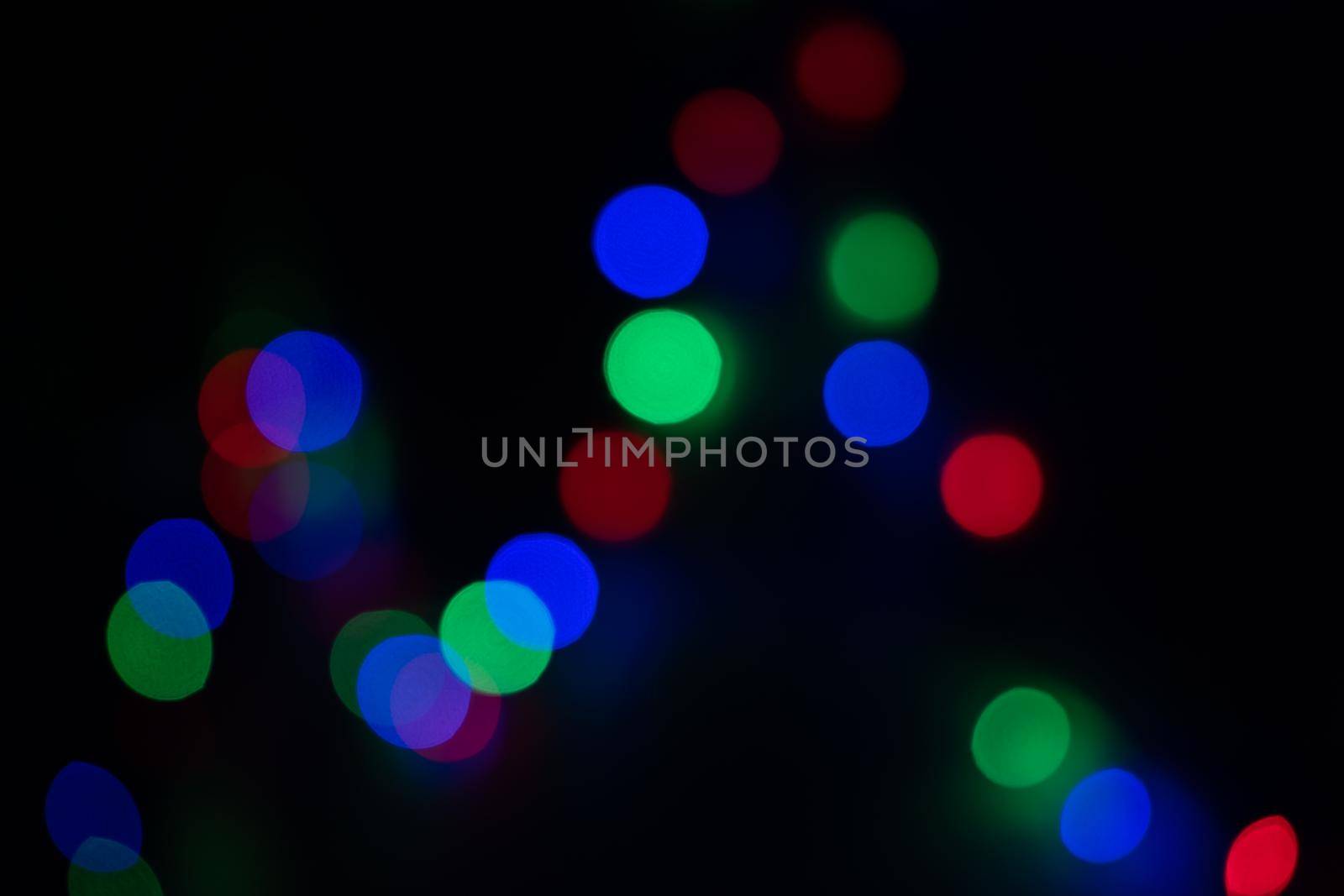 Defocused bokeh lights on black background, an abstract naturally blurred backdrop for Christmas eve or birthday party. Festive light texture. Colorful garland in blur. Overlay effect for design