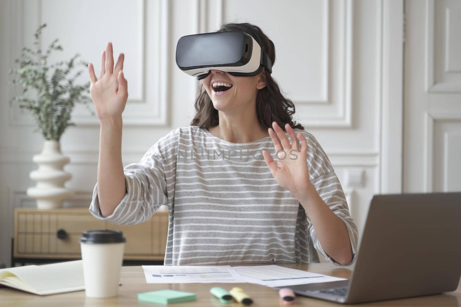 Excited amazed woman wearing VR glasses enjoying amazing virtual reality experience at work by vkstock