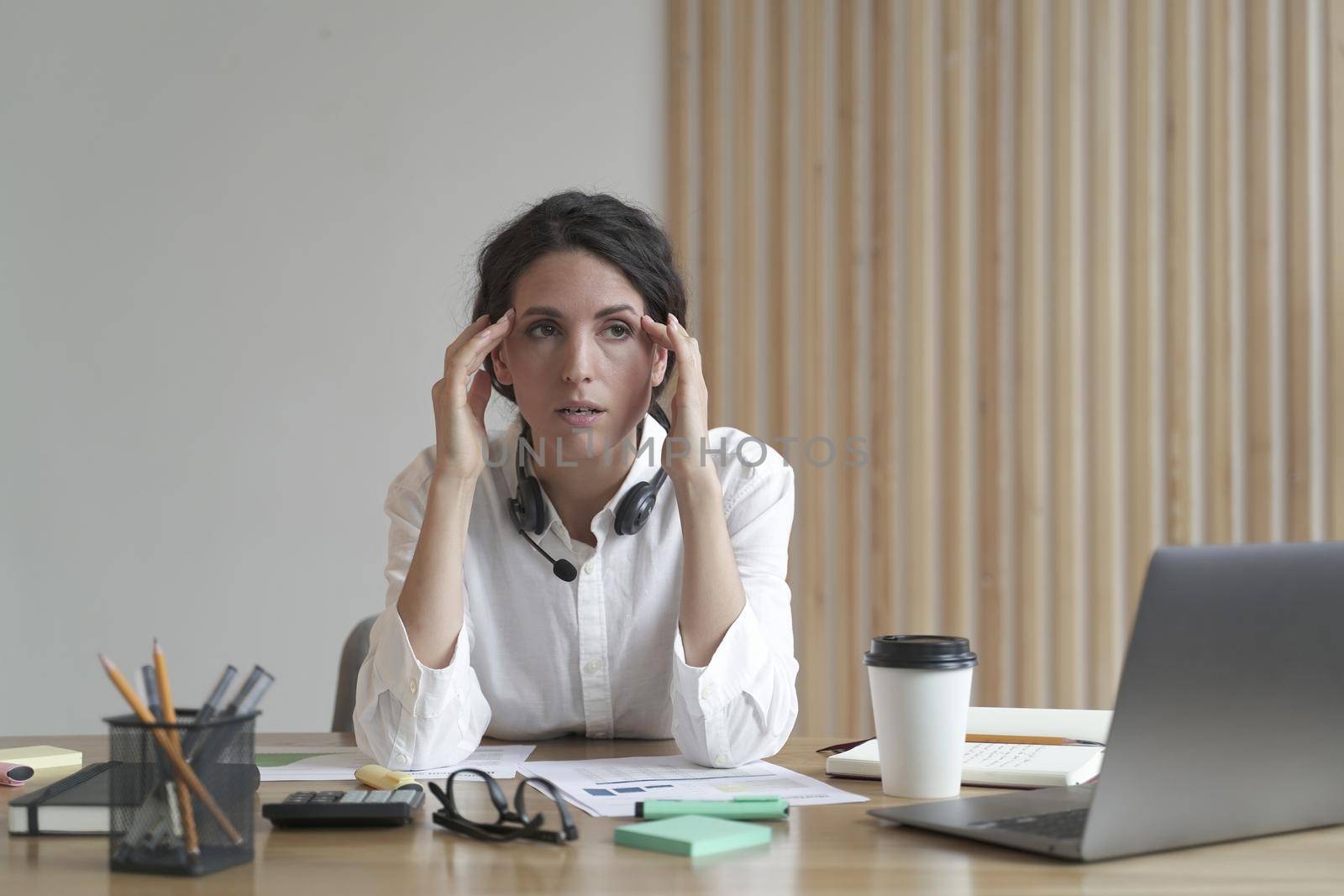 Frustrated business woman feeling tired while sitting at table in office, thinking about problem solution at work, young stressed italian woman employee suffering from headache after hard working day