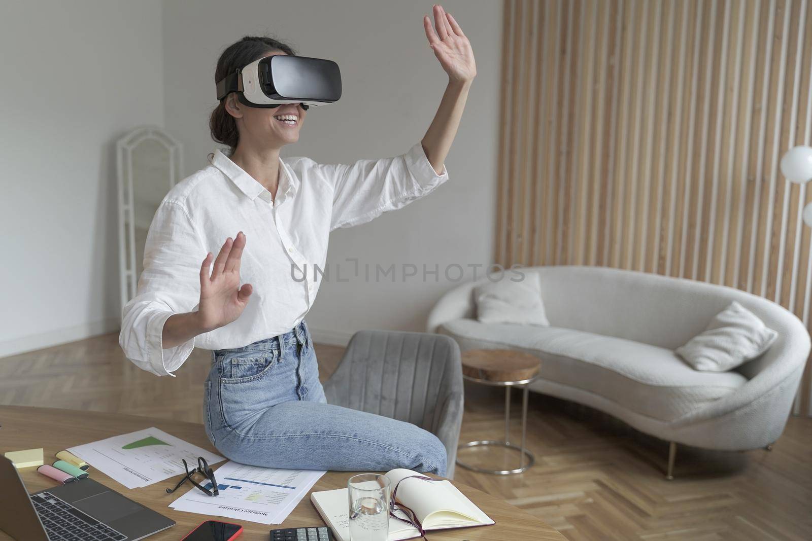 Businesswoman in VR headset on head touching 3d objects while working in modern office by vkstock