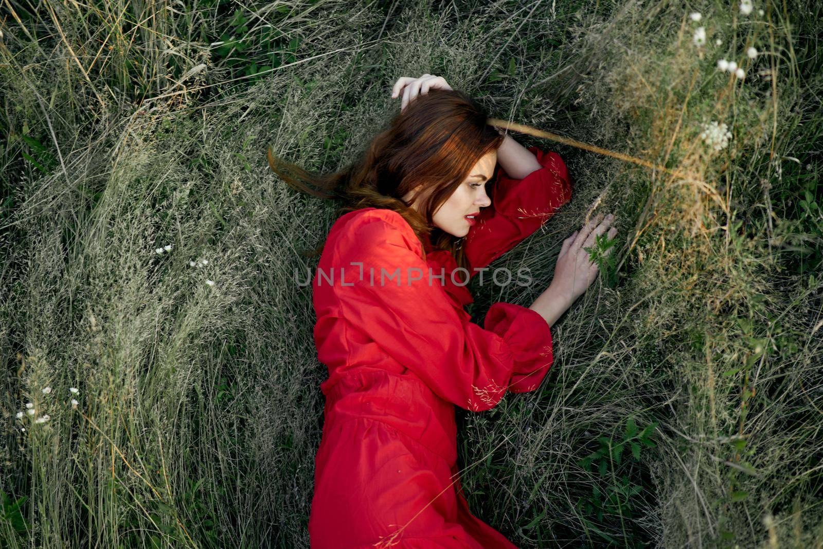 pretty woman in red dress lies on the grass posing top view. High quality photo