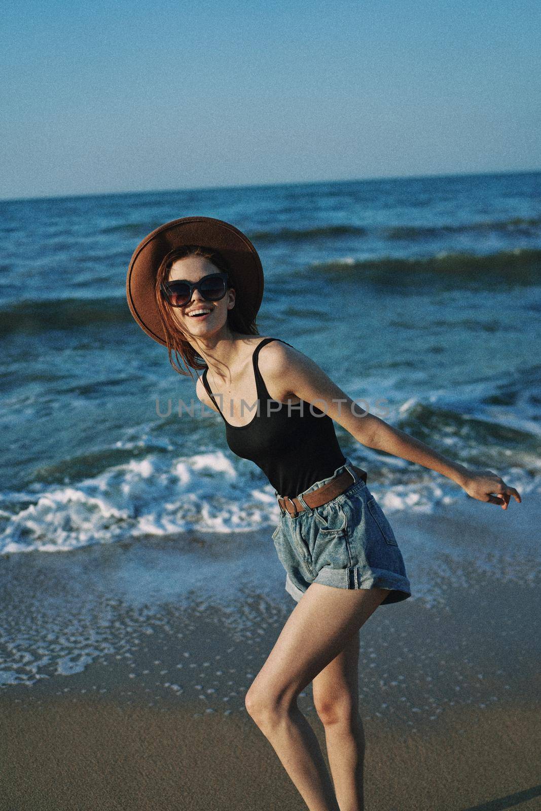 cheerful woman in sunglasses and a hat walks along the ocean. High quality photo