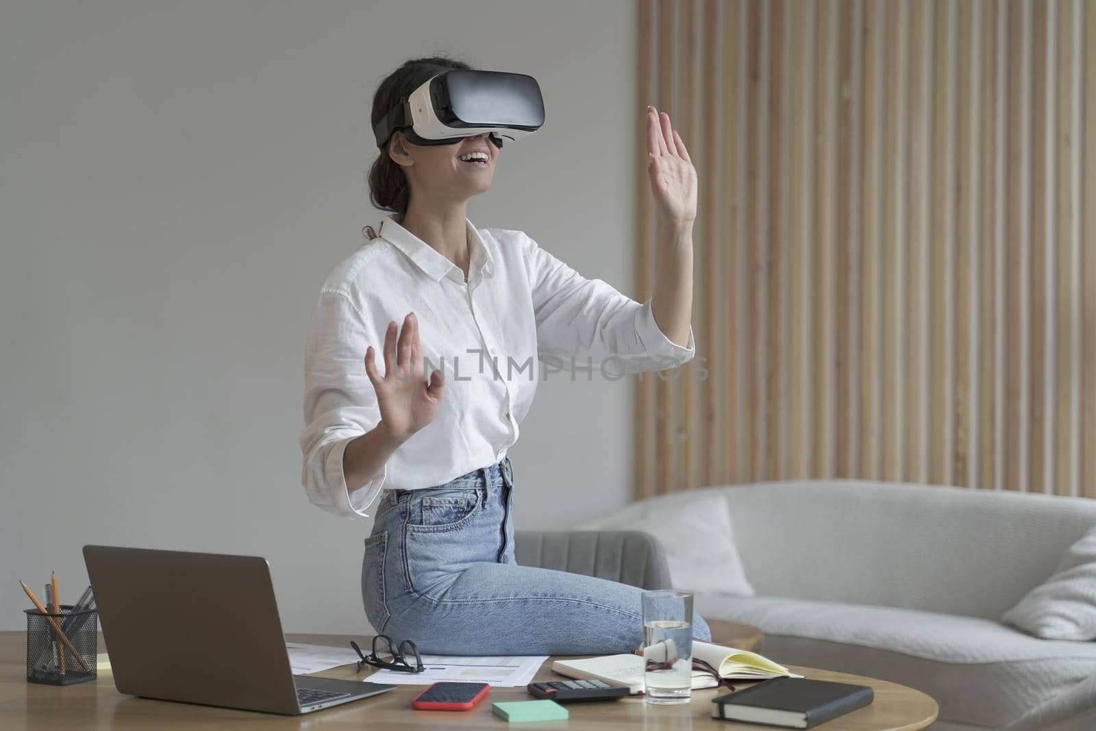 Photo of businesswoman in elegant formal clothes sitting in office and using VR technologies at work, female employee wearing 3d goggles engaged in virtual conference with colleagues