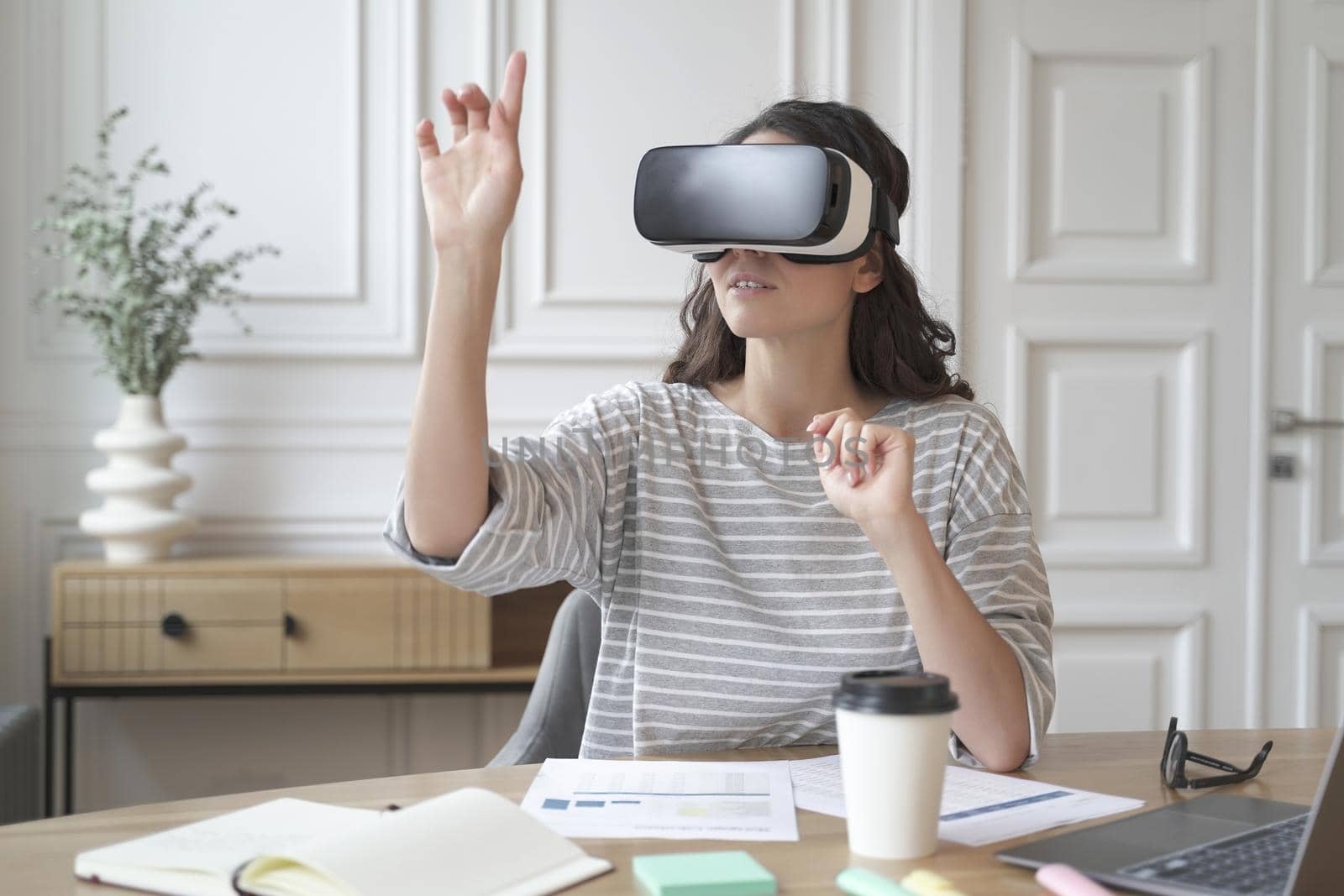 Young focused woman wearing virtual reality headset watching 360 degree content at work by vkstock