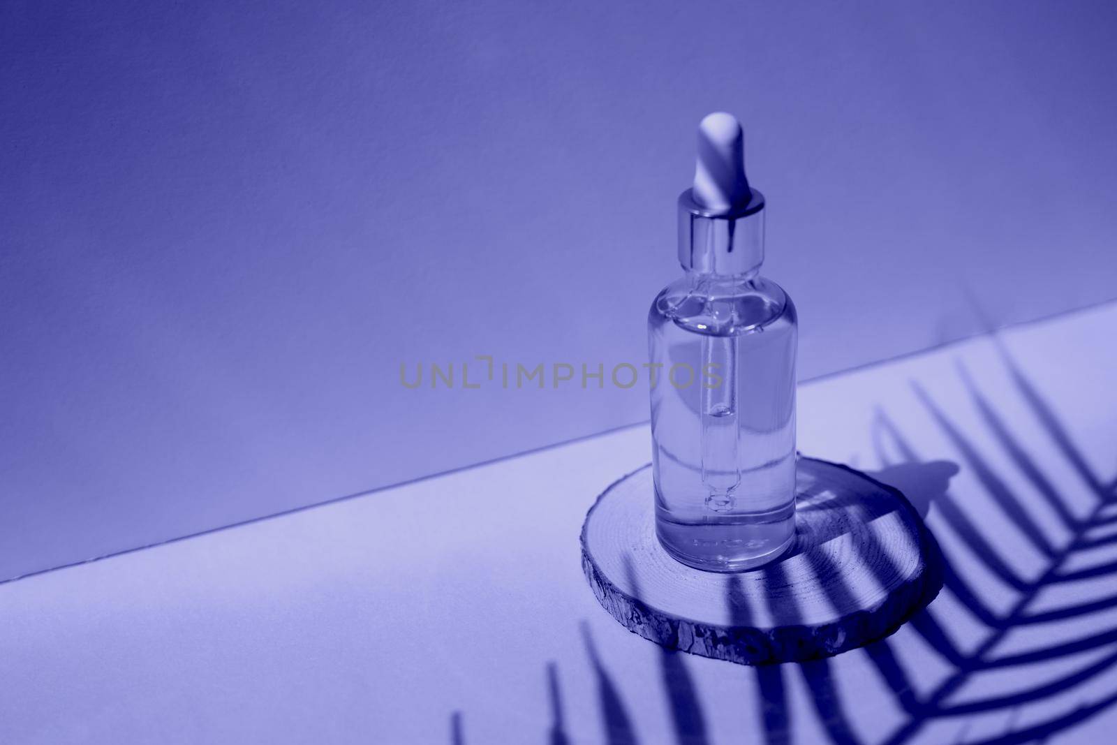 Cosmetic bottle with facial serum on a wooden podium. The concept of zero waste and ecology. A hard shadow from a palm leaf. Demonstrating the colors of 2022 - Very Peri