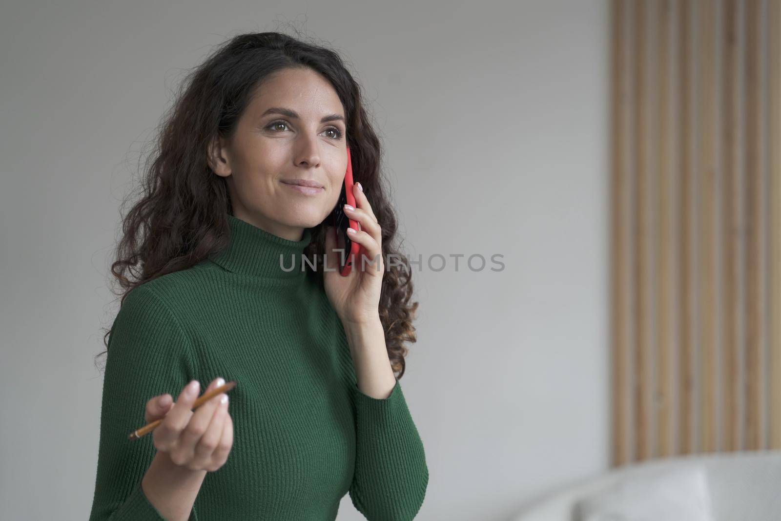 Attractive Spanish young businesswoman enjoying telephone conversation, using smartphone at work by vkstock