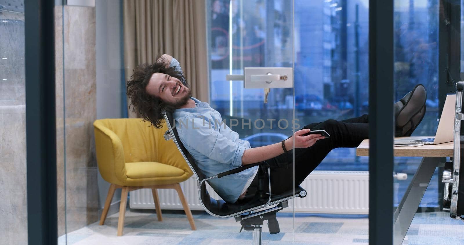 Full length of a relaxed casual young businessman sitting with legs on desk at office