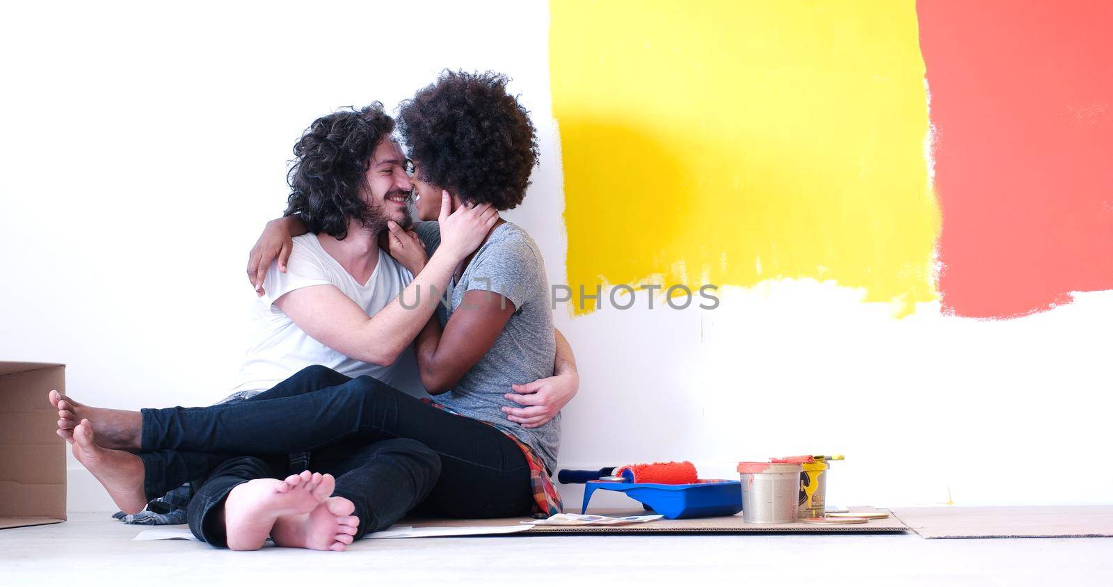 Happy young multiethnic couple relaxing after painting a room in their new house on the floor