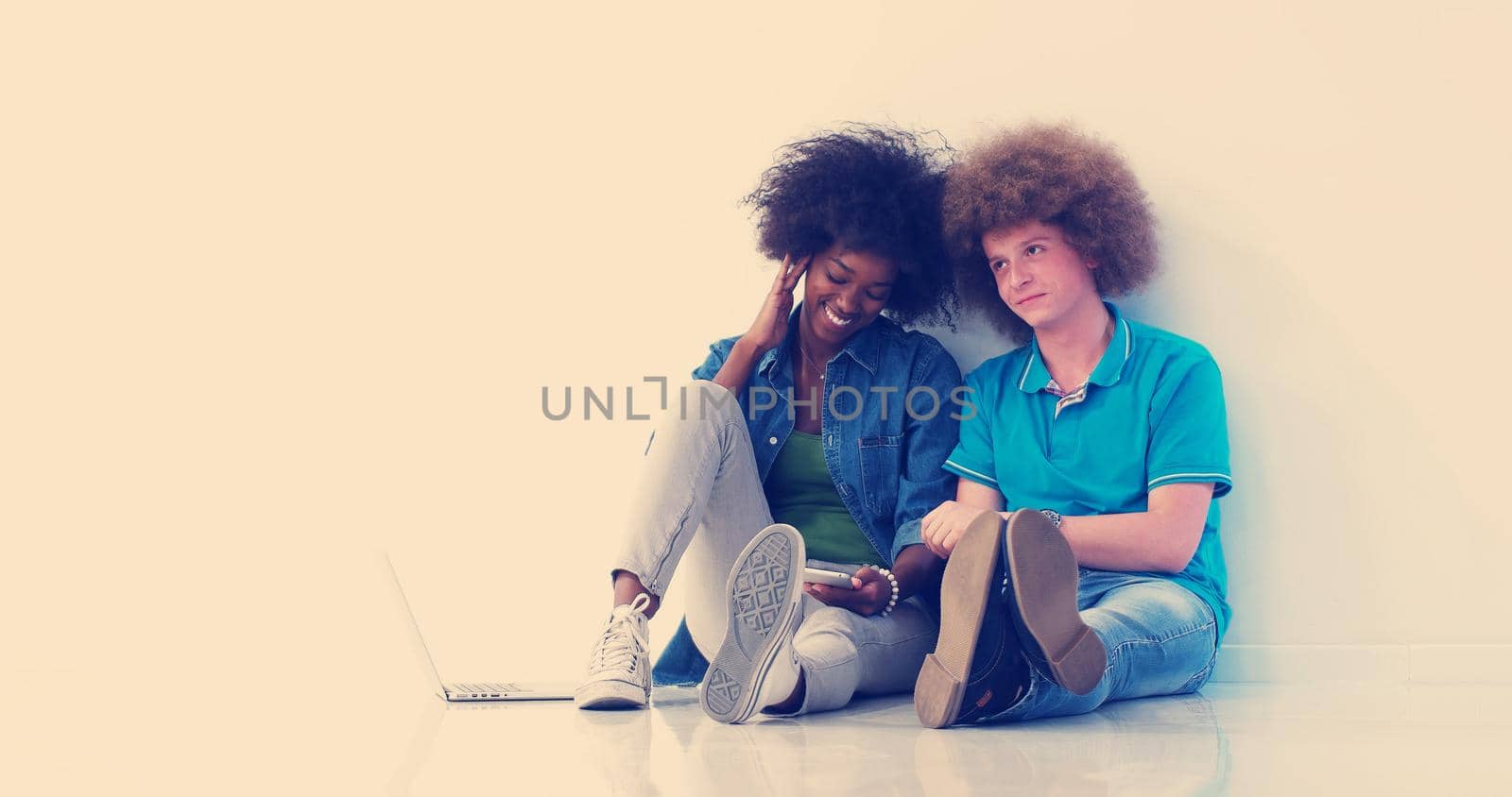 multiethnic couple sitting on the floor using a laptop and tablet by dotshock