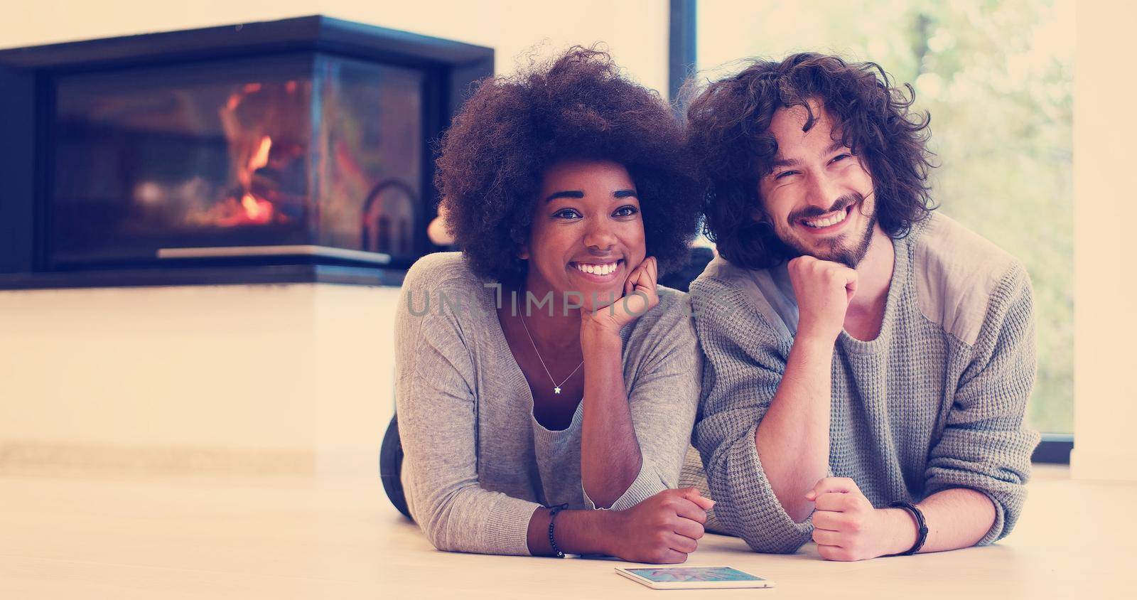 beautiful young multiethnic couple lying on the floor of their luxury home in front of fireplace at autumn day