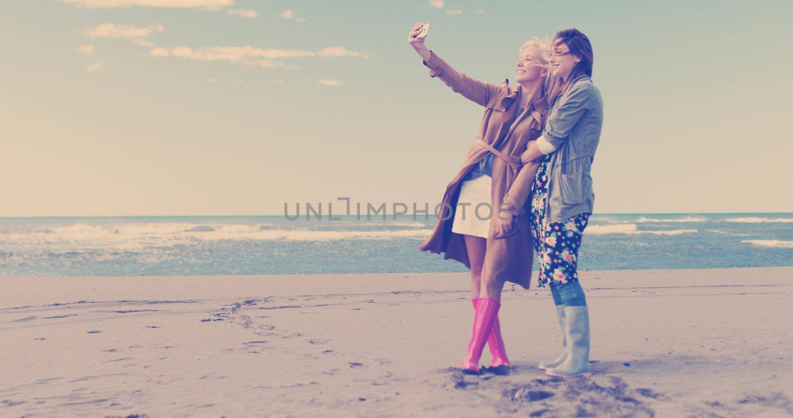 Friends making selfie. two beautiful young women making selfie at autumn day on the beach