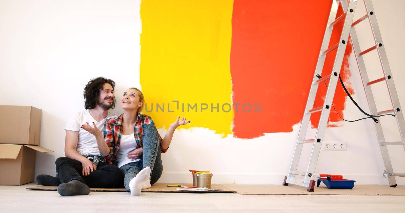 Happy young couple relaxing after painting a room in their new house on the floor