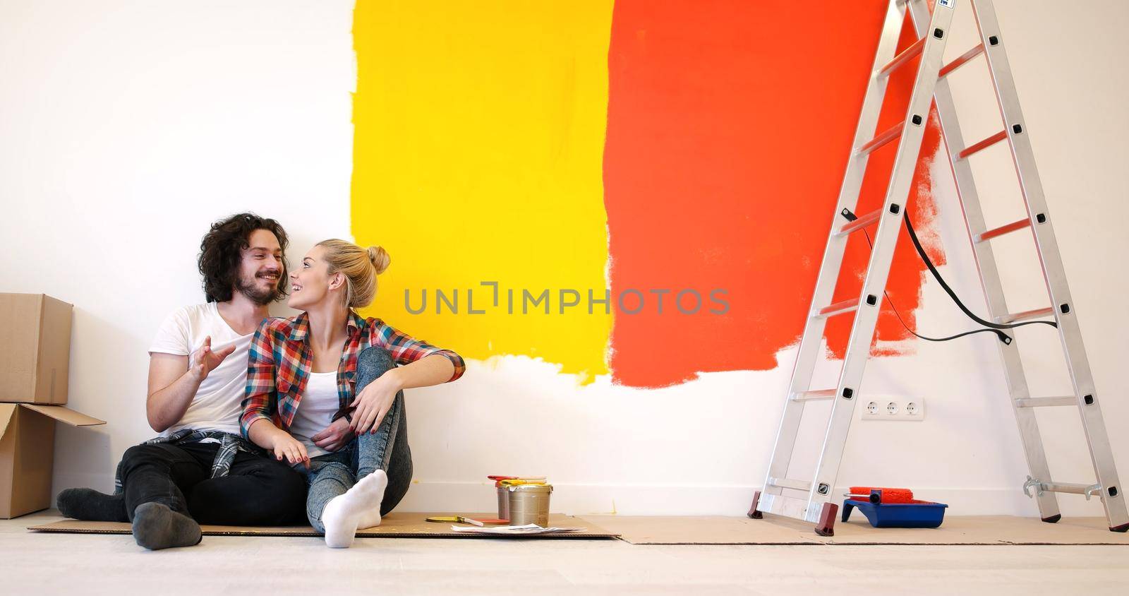 Happy young couple relaxing after painting a room in their new house on the floor