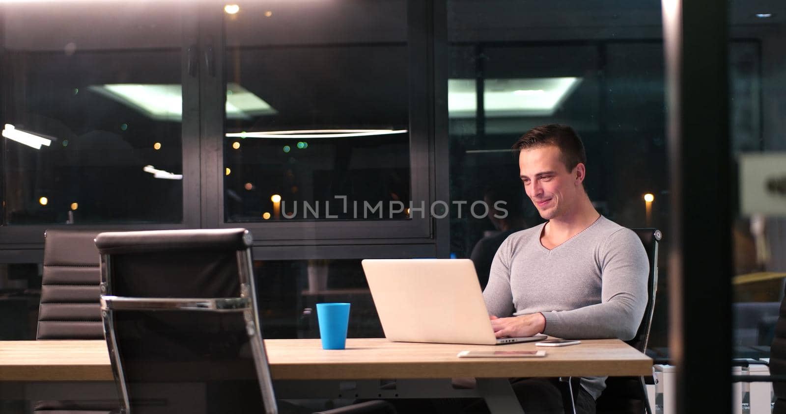 Young man working on laptop at night in dark office. The designer works in the later time.