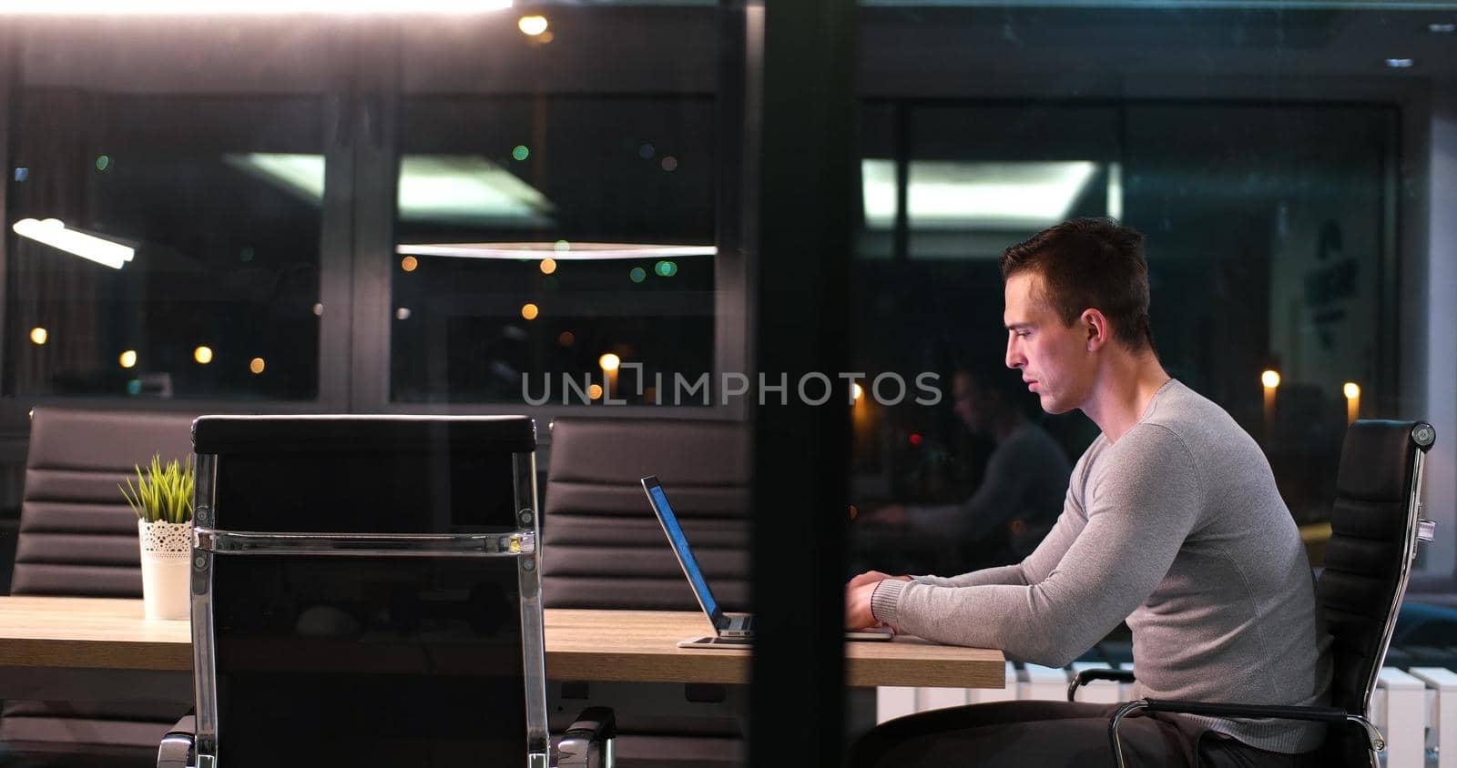 Young man working on laptop at night in dark office. The designer works in the later time.