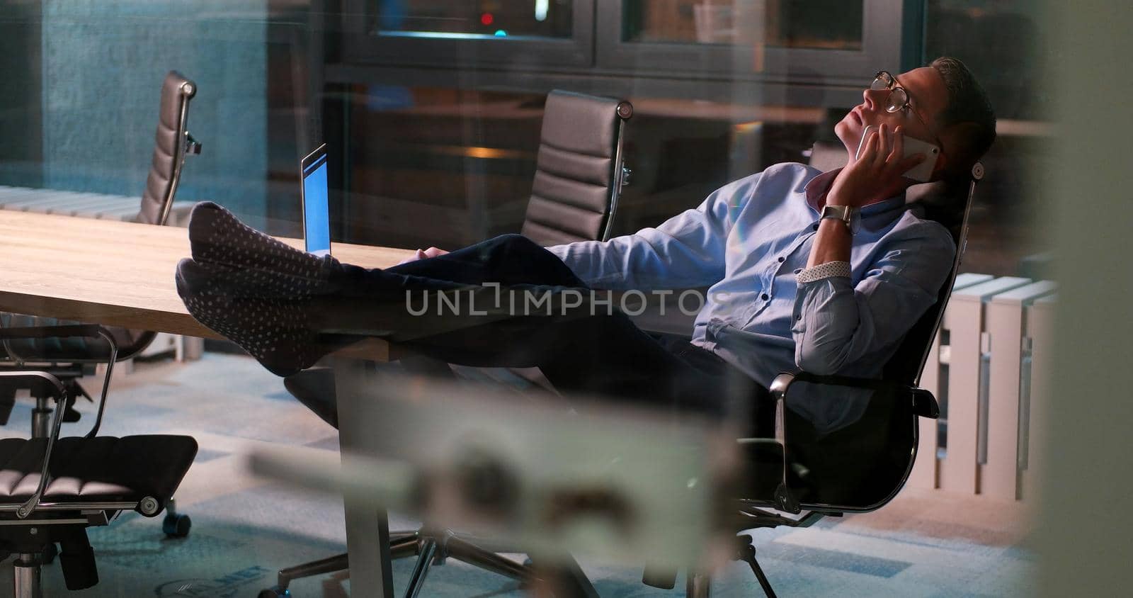 Full length of a relaxed casual young businessman sitting with legs on desk at night office