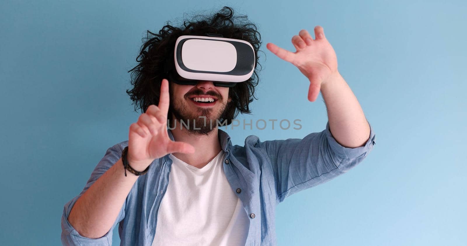 Happy man getting experience using VR headset glasses of virtual reality, isolated on blue background