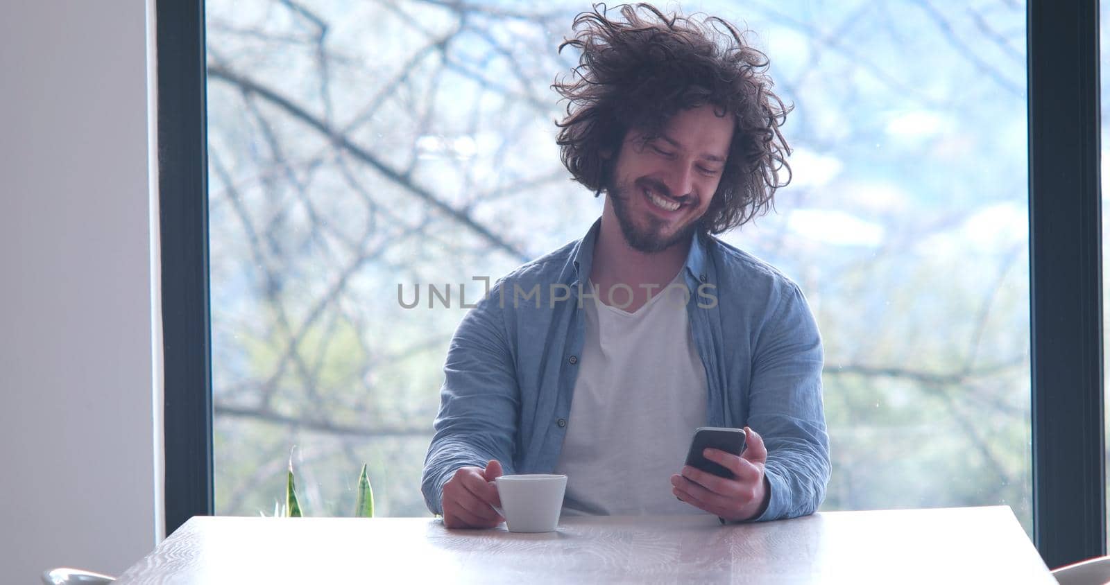 Handsome casual young man drinking coffee and using a mobile phone at  home