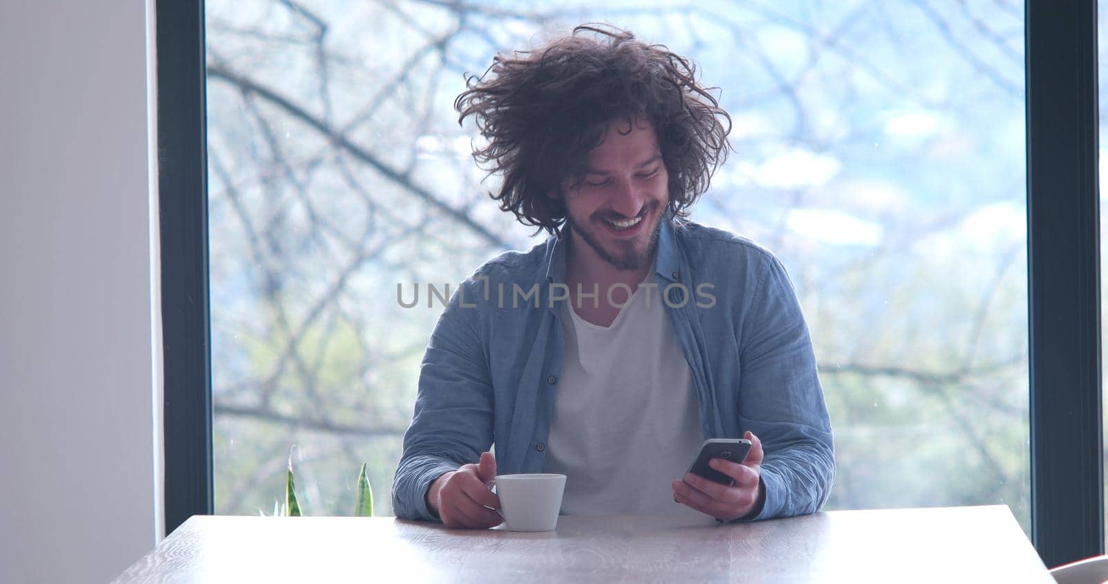 Handsome casual young man drinking coffee and using a mobile phone at  home