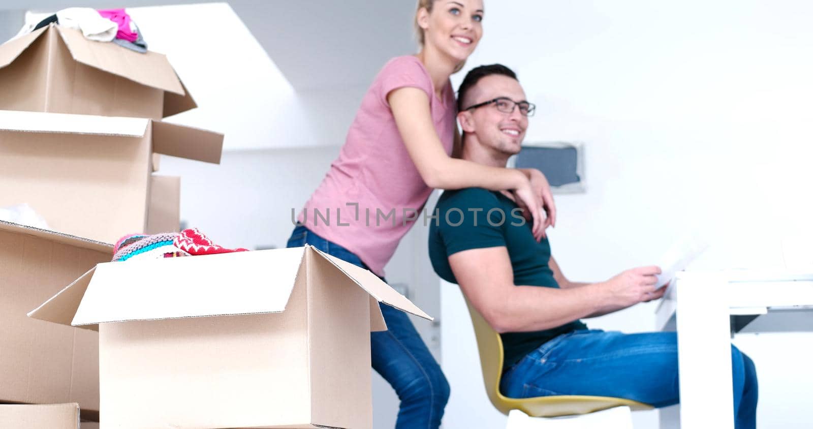 Young couple moving in a new home. Man and woman at the table using notebook laptop computer and plans with boxes around them