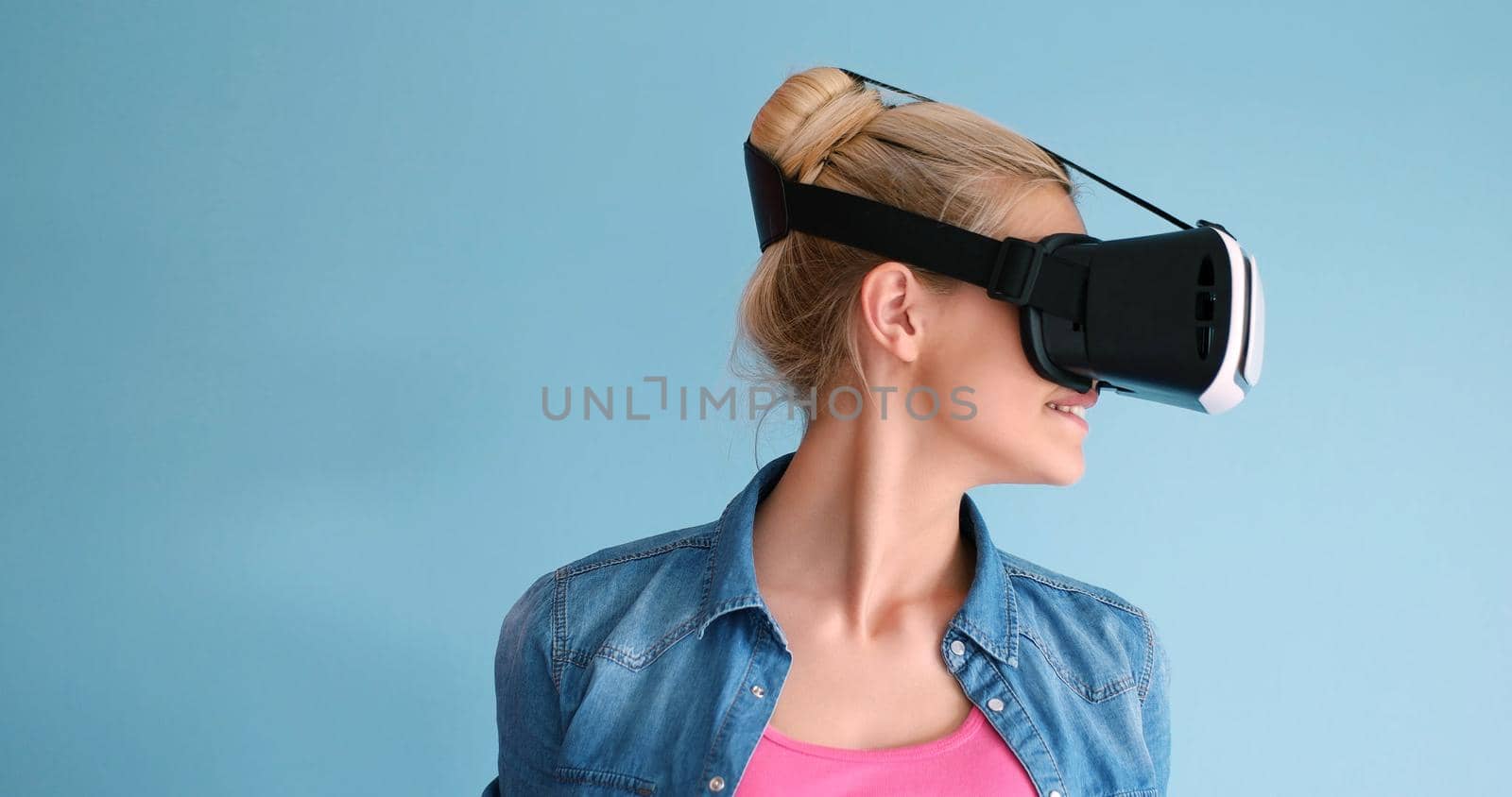 Happy girl getting experience using VR headset glasses of virtual reality, isolated on blue background