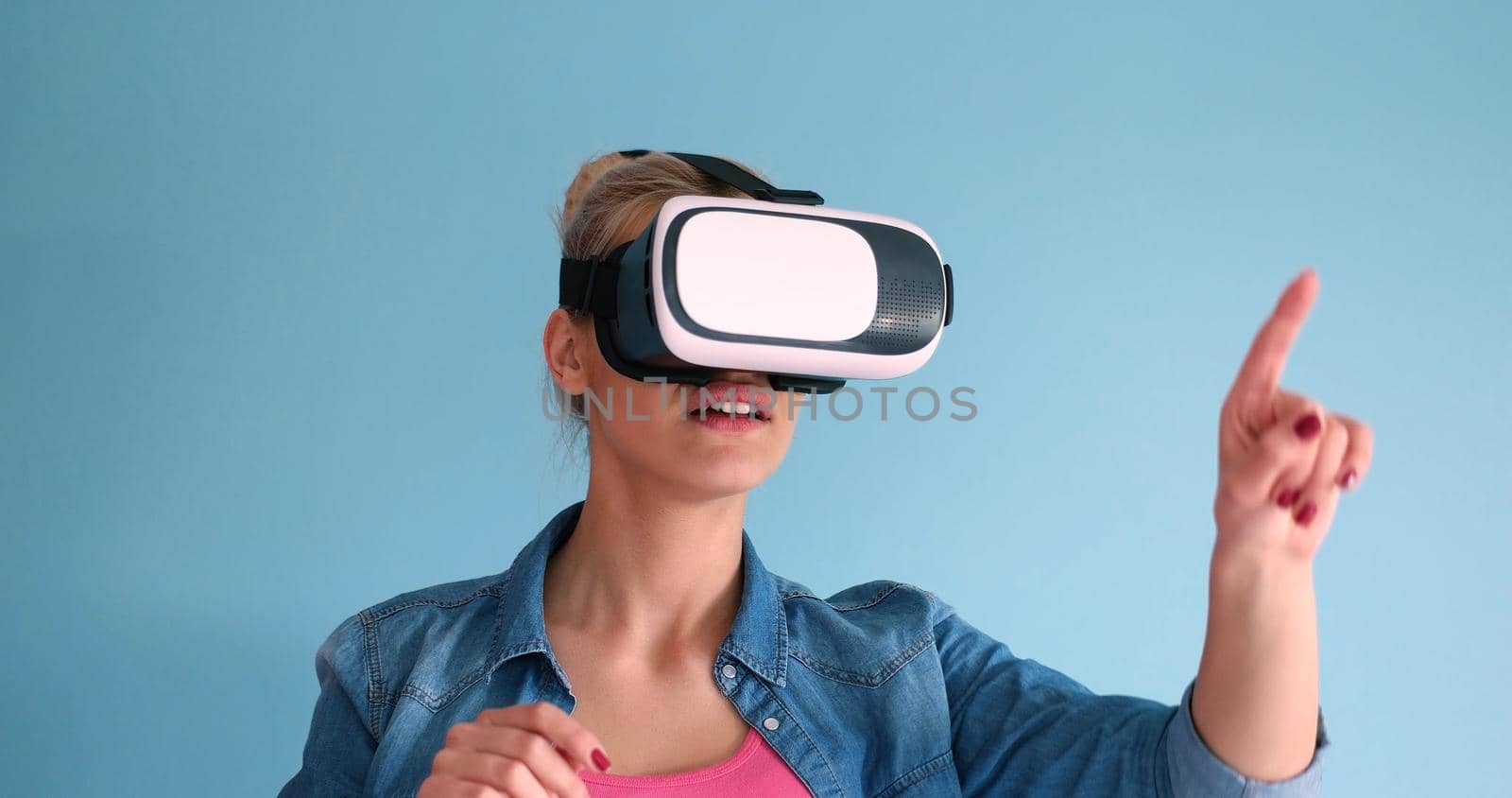 Happy girl getting experience using VR headset glasses of virtual reality, isolated on blue background