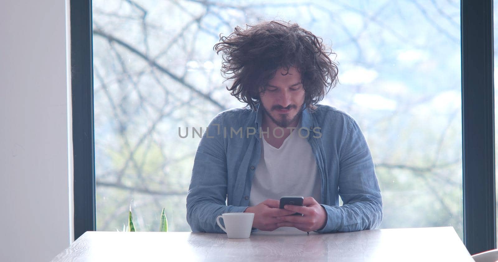 Handsome casual young man drinking coffee and using a mobile phone at  home