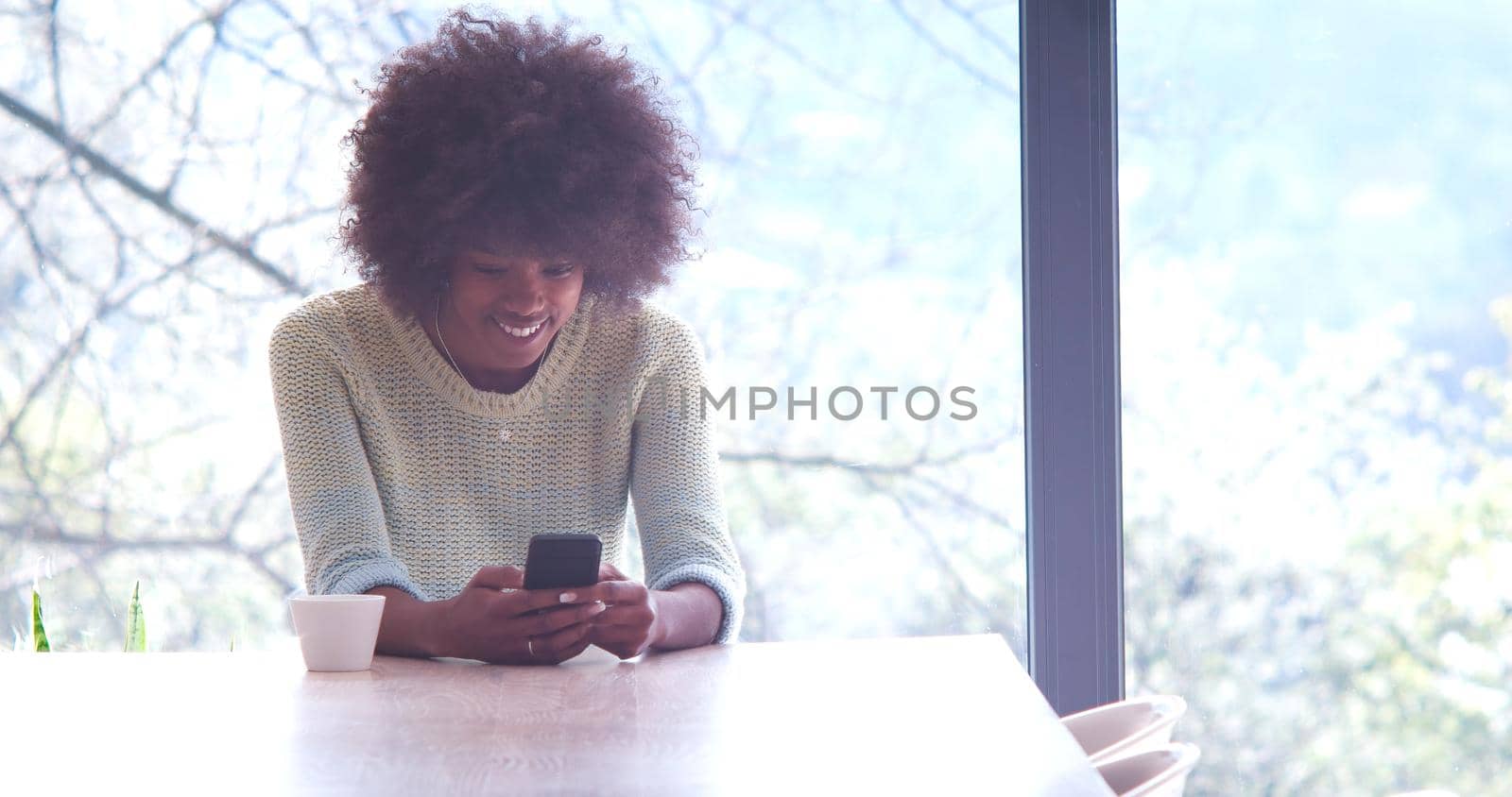 Handsome young african american woman drinking coffee and using a mobile phone at  home