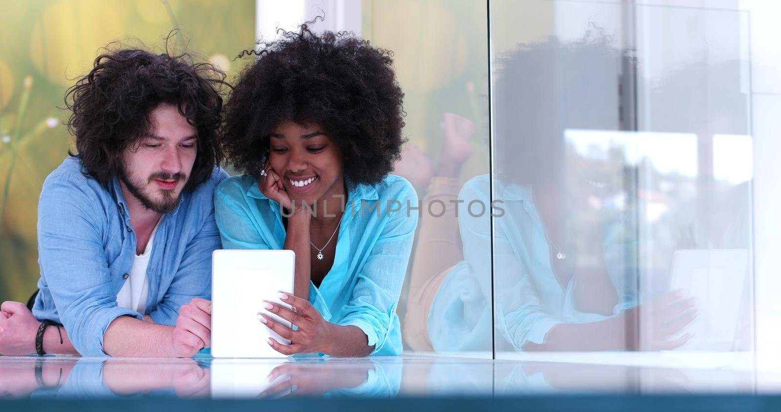 Happy young multiethnic couple lying on floor having fun using Digital Tablet