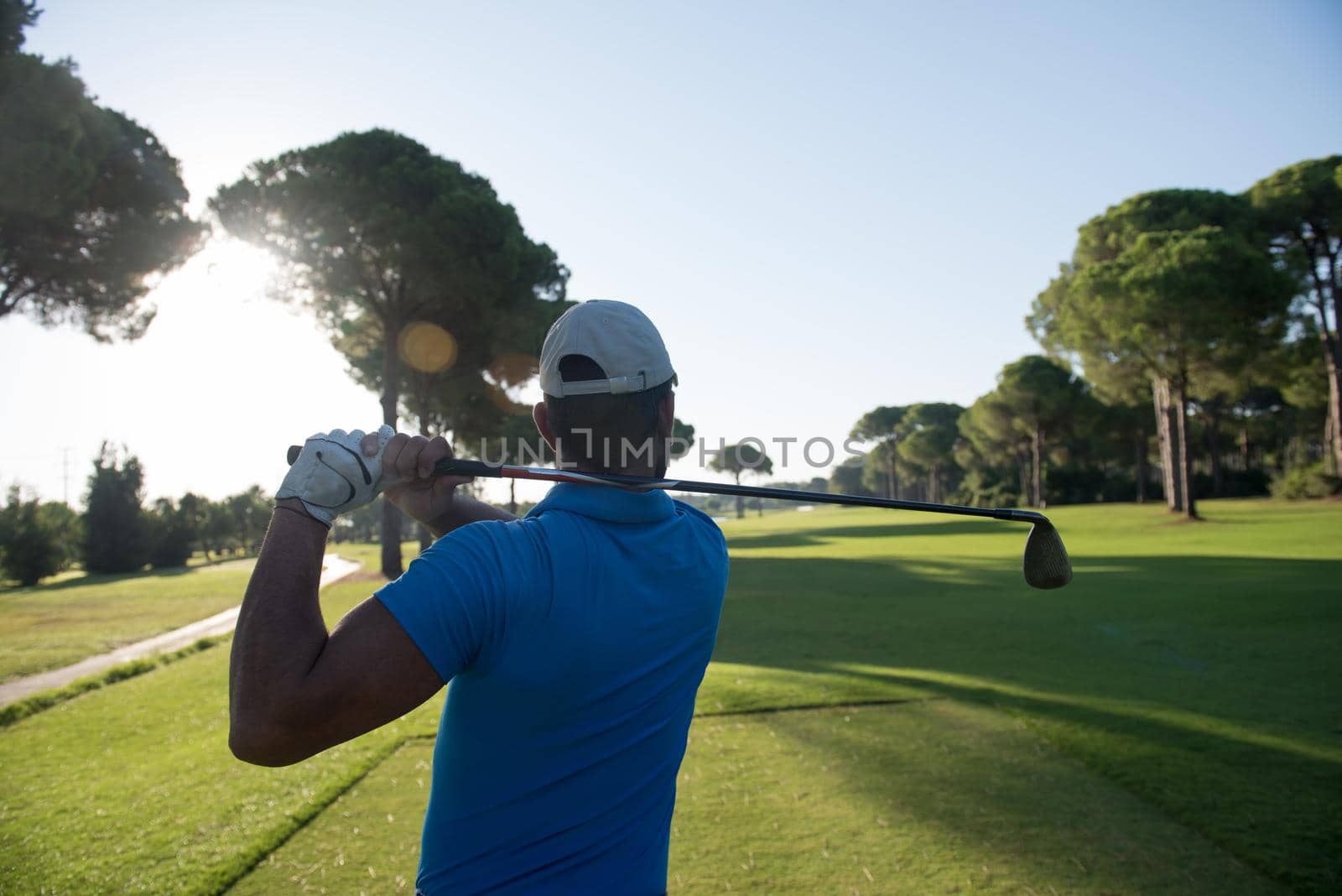 golf player hitting shot with club on course at beautiful morning with sun flare in background