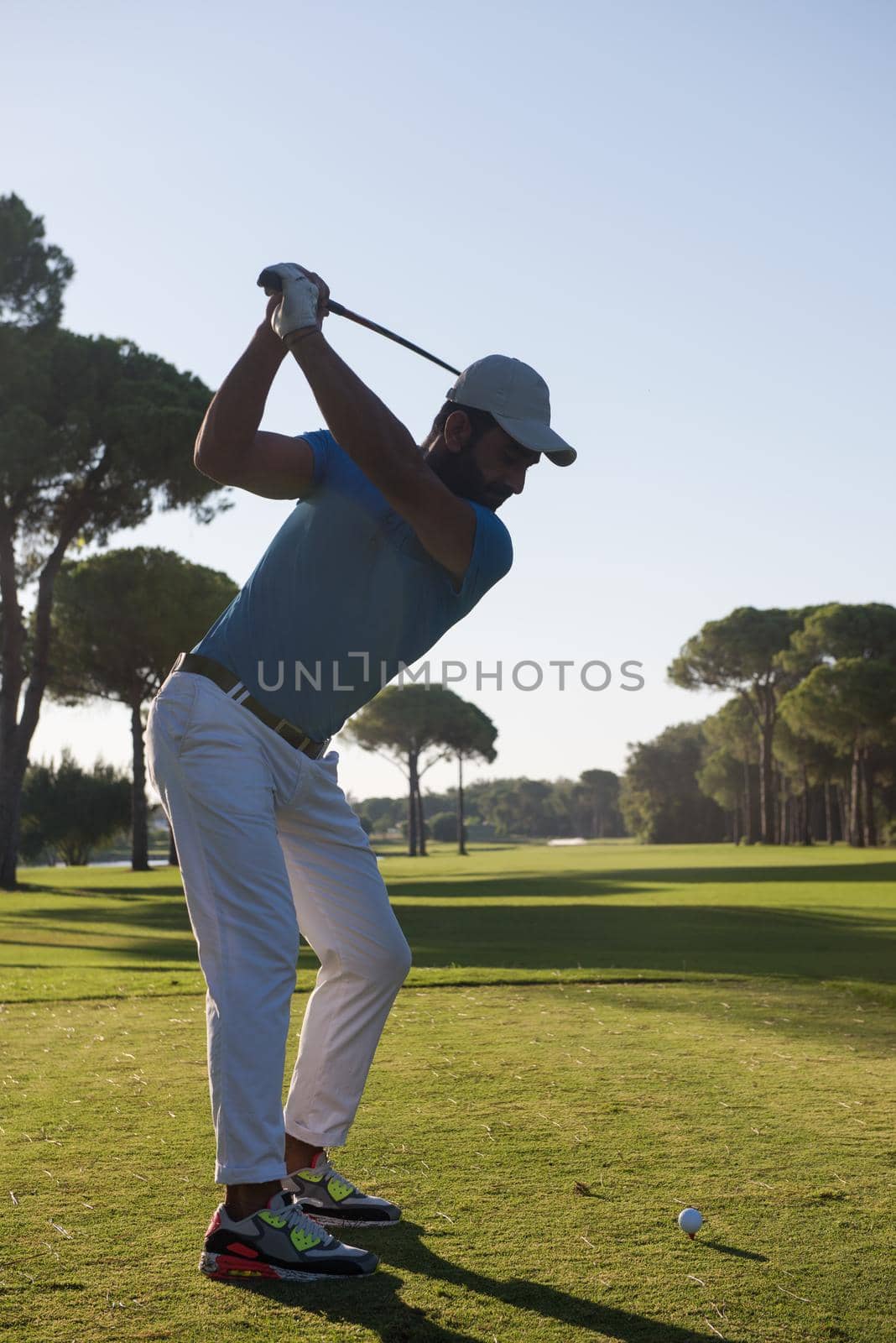 golf player hitting shot with club on course at beautiful morning with sun flare in background