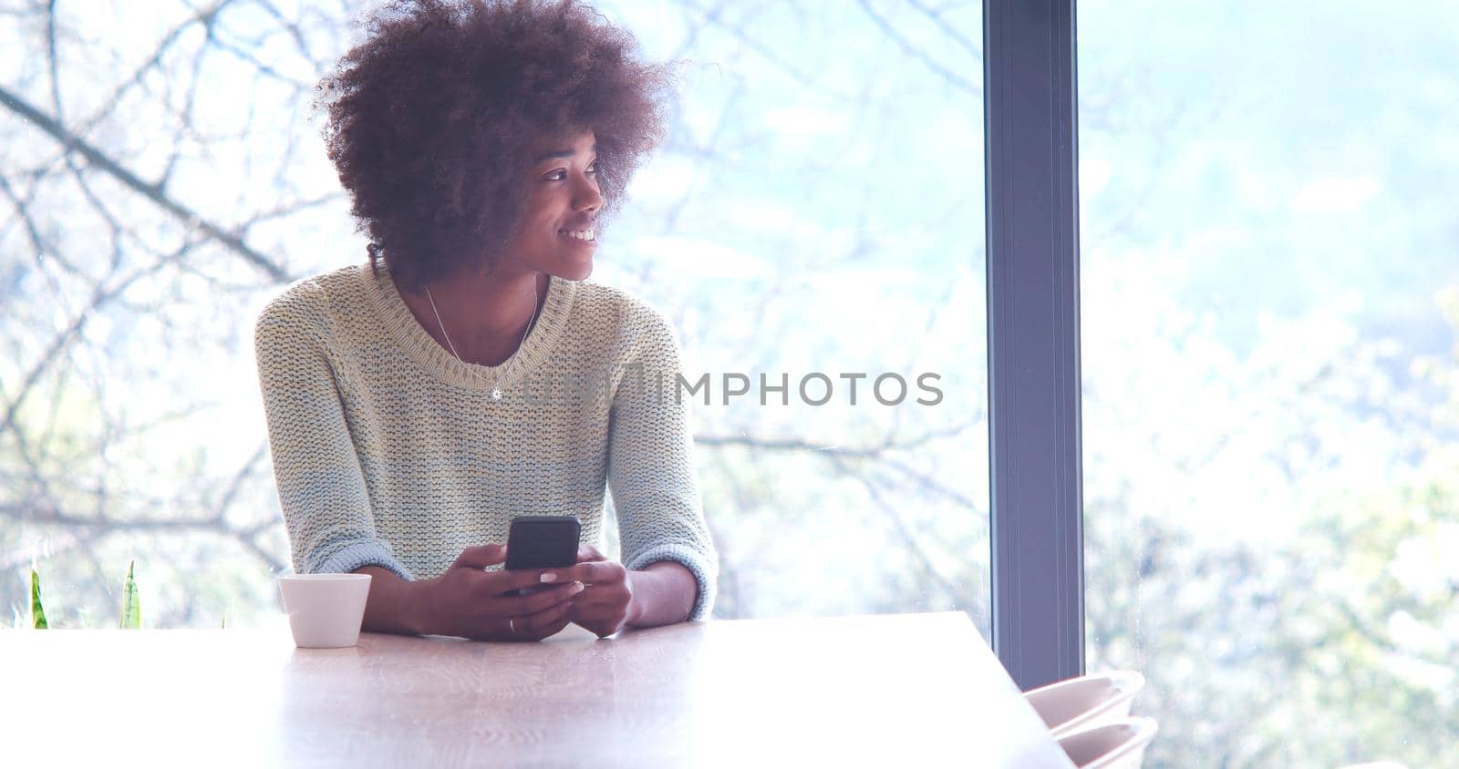 Handsome young african american woman drinking coffee and using a mobile phone at  home