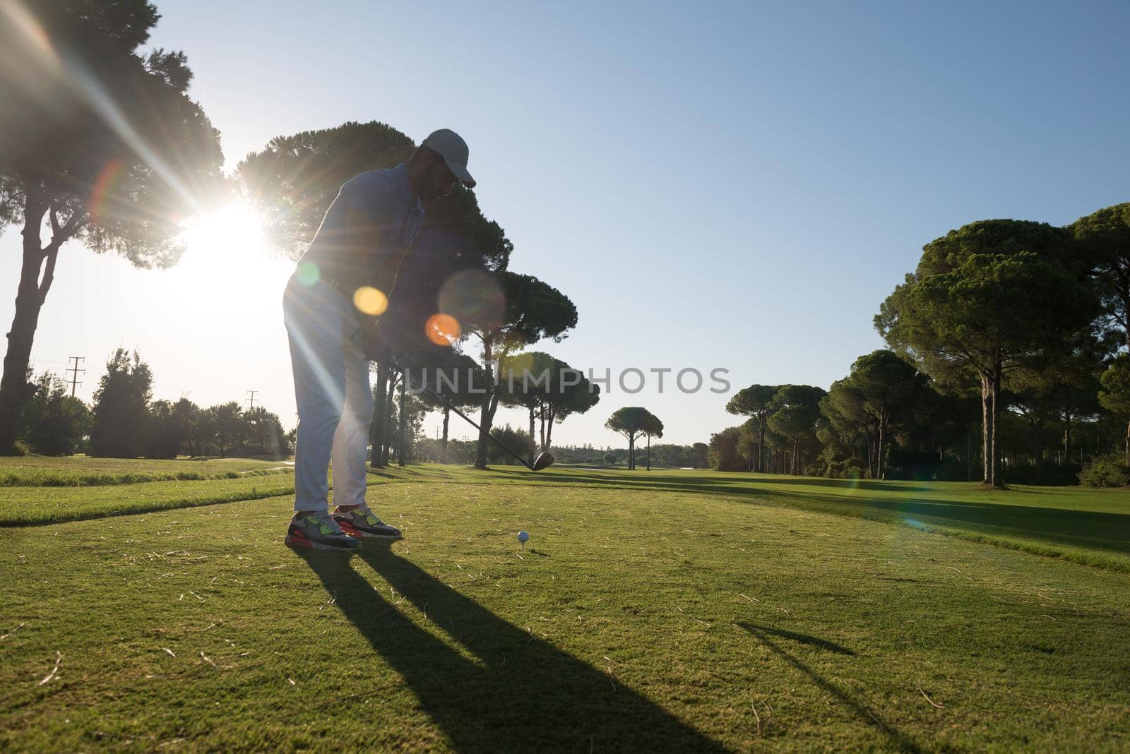 golf player hitting shot with club on course at beautiful morning with sun flare in background