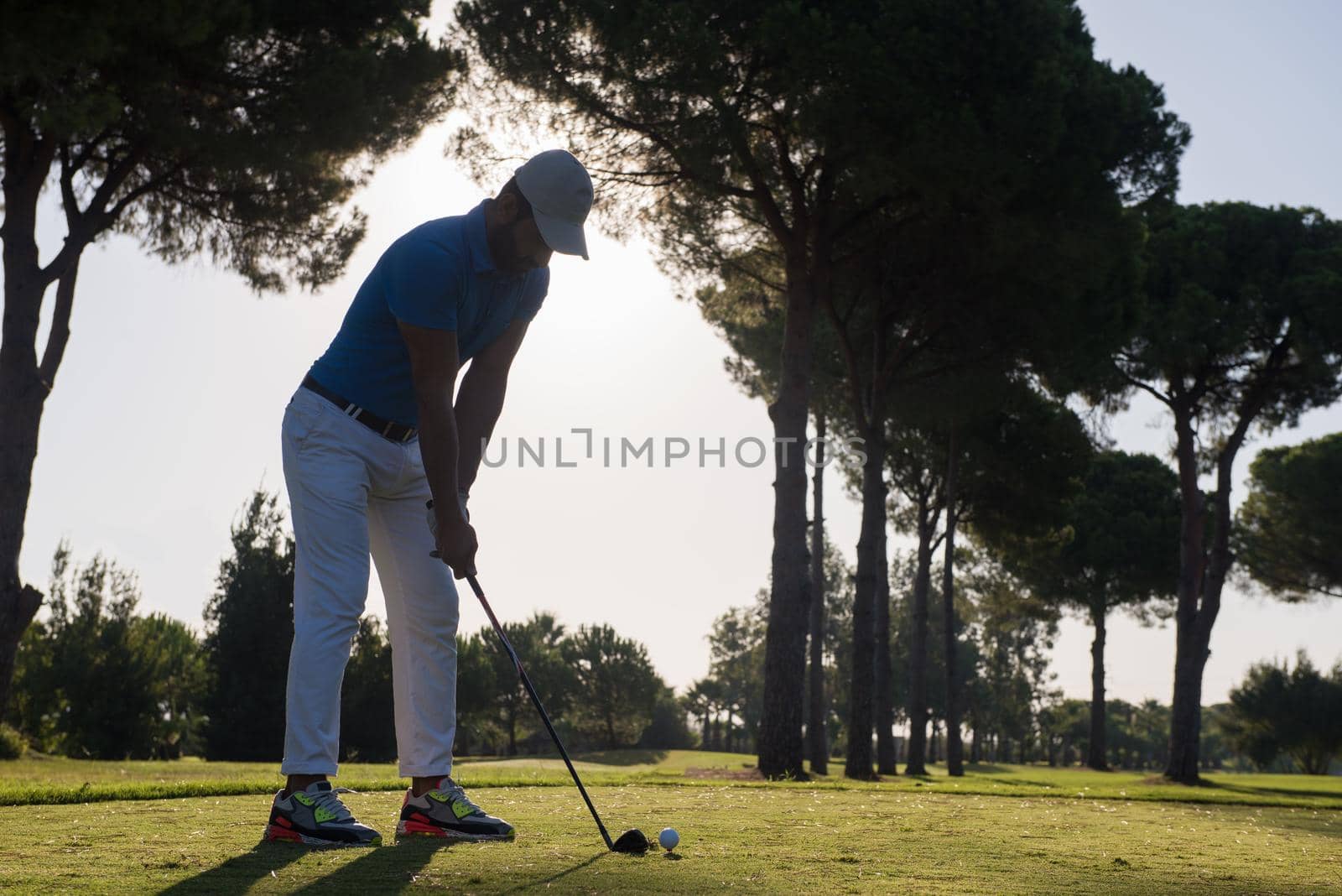 golf player hitting shot with club on course at beautiful morning with sun flare in background