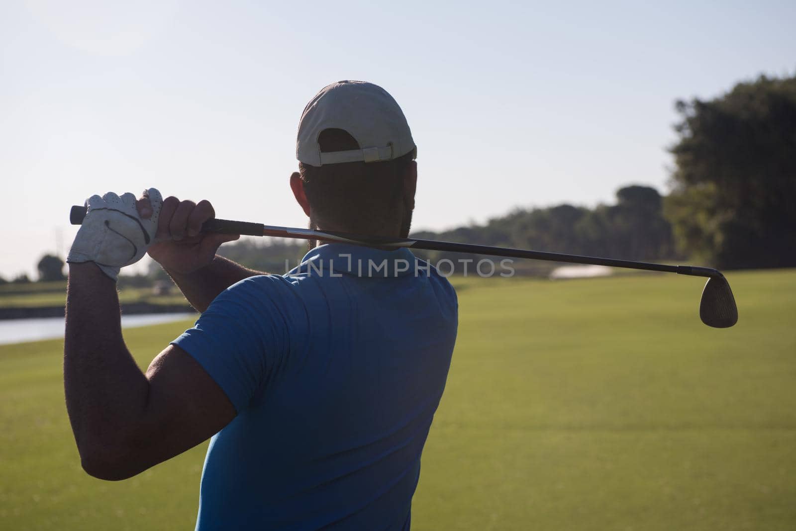 golf player hitting shot with club on course at beautiful morning with sun flare in background