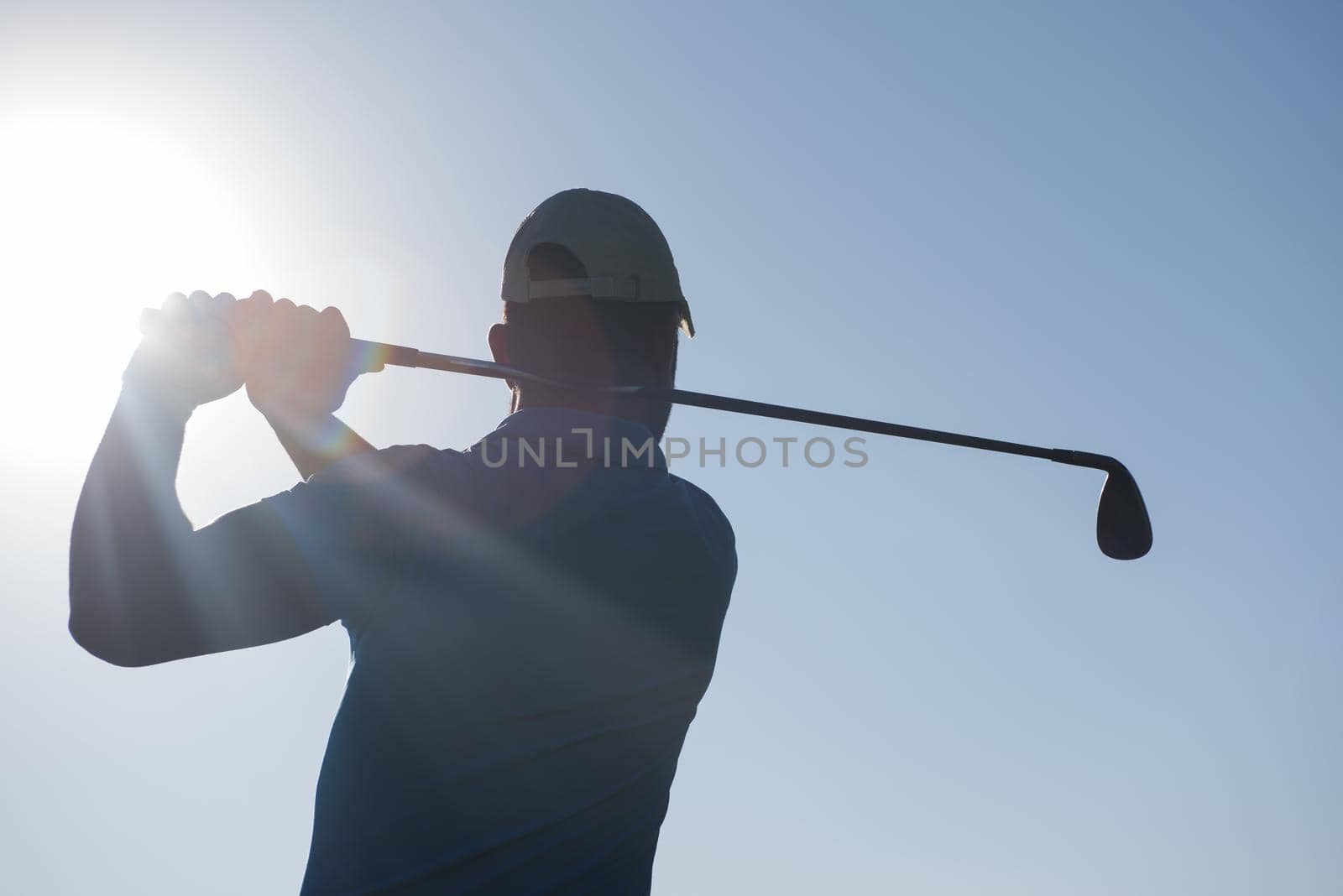 golf player hitting shot with club on course at beautiful morning with sun flare in background