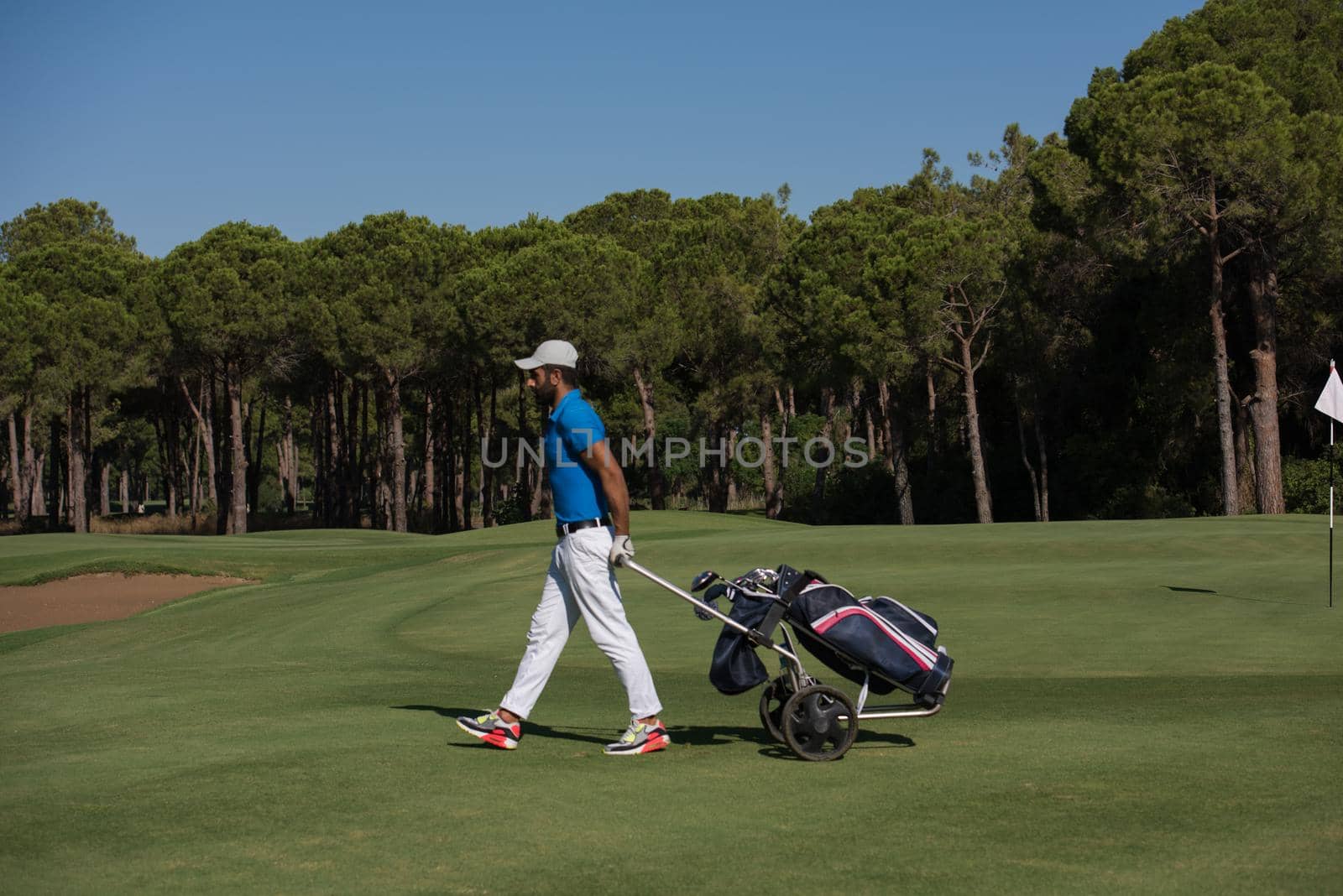 handsome middle eastern golf playerwalking with wheel bag at course on beautiful  sunny day