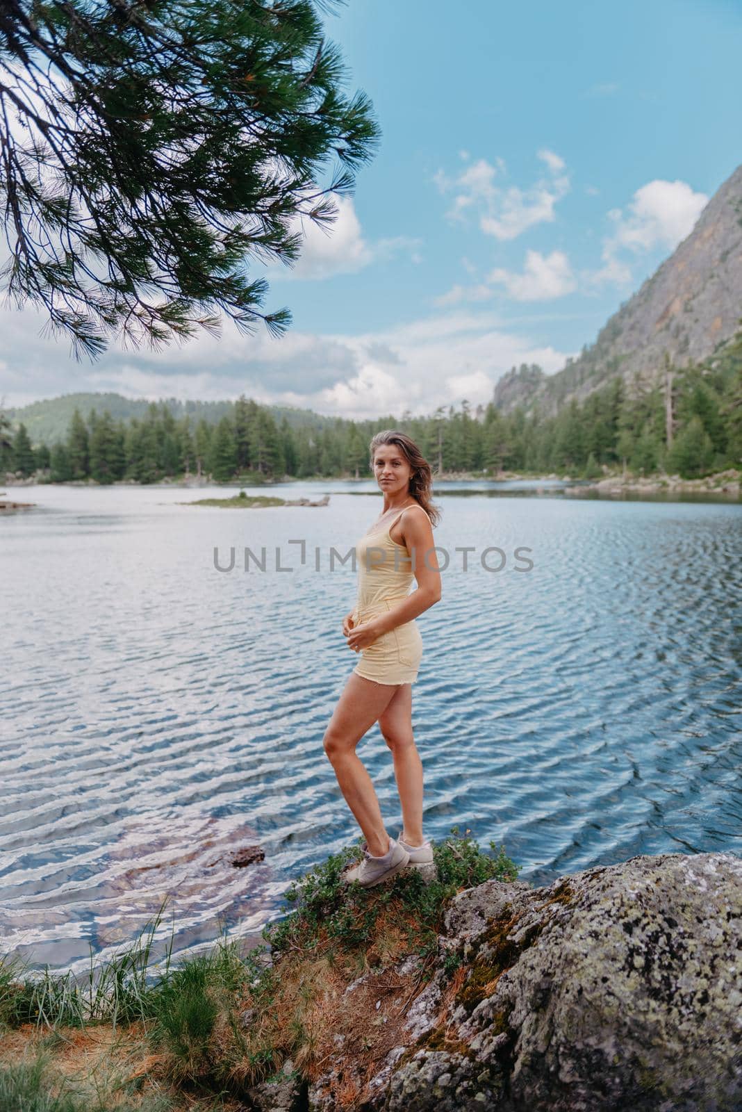 Tourist girl enjoys the magical view of the lake, coniferous forest and magical view sitting on big stone on the shore of a turquoise lake in the mountains. Hiking in the Natural Park. Cute girl tourist sitting on a large stone by the lake. The water is clear, stones are visible under the water. by Andrii_Ko