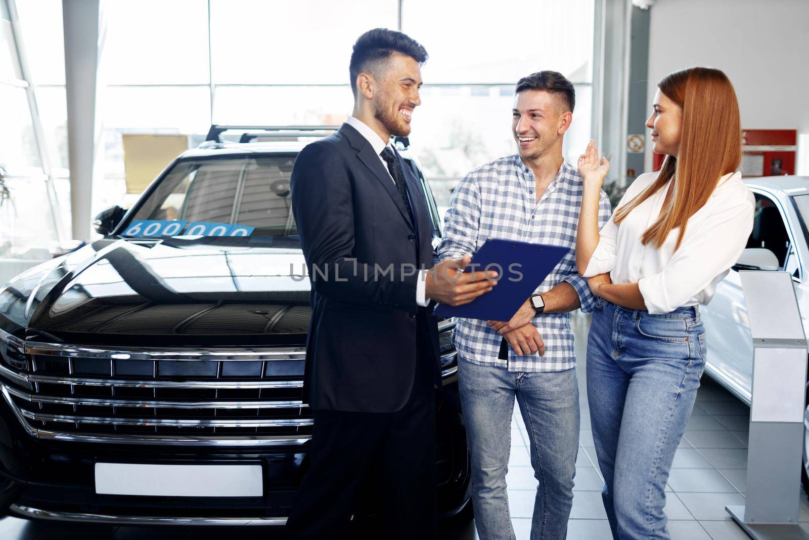 Man car salesman telling about the features of the new car to the couple by Fabrikasimf