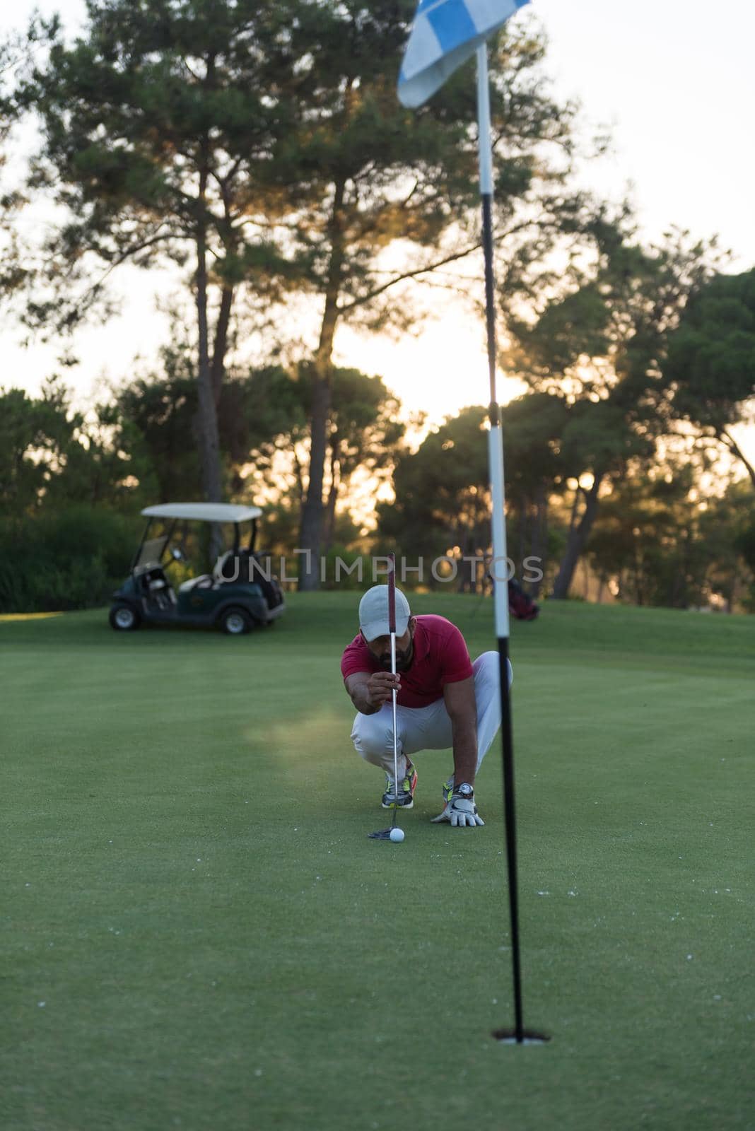 golf player aiming shot with club on course at beautiful sunset with sun flare in background