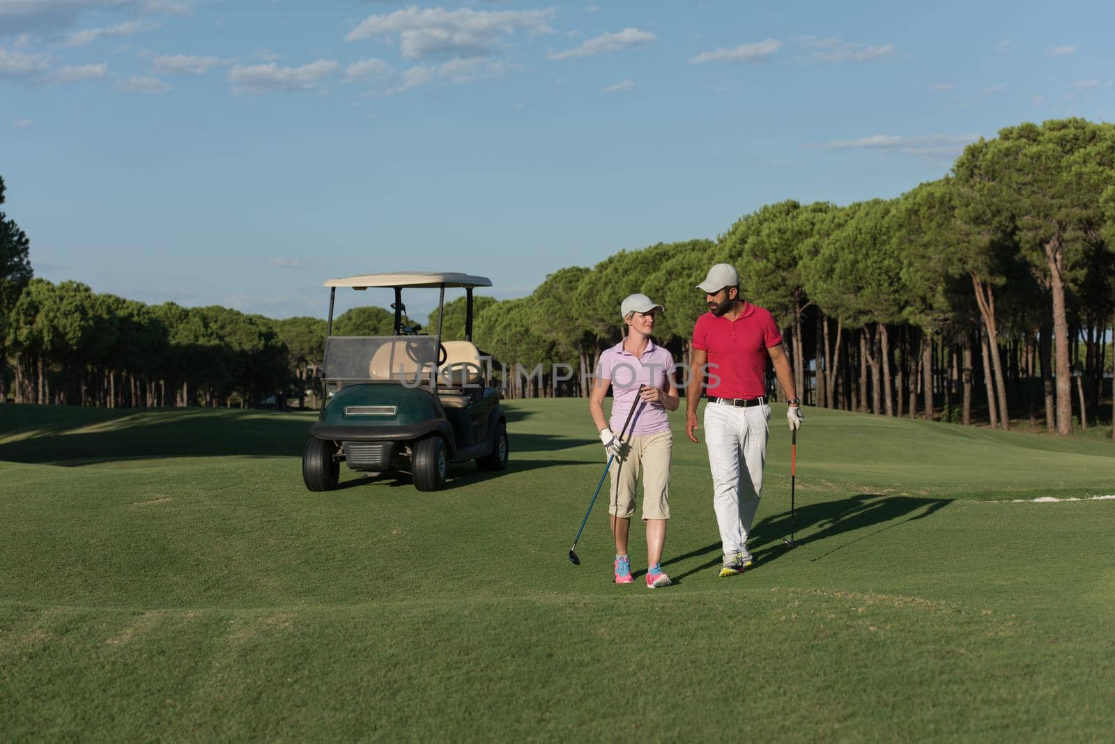 young couple walking to next hole on golf course. man carrying golf bag