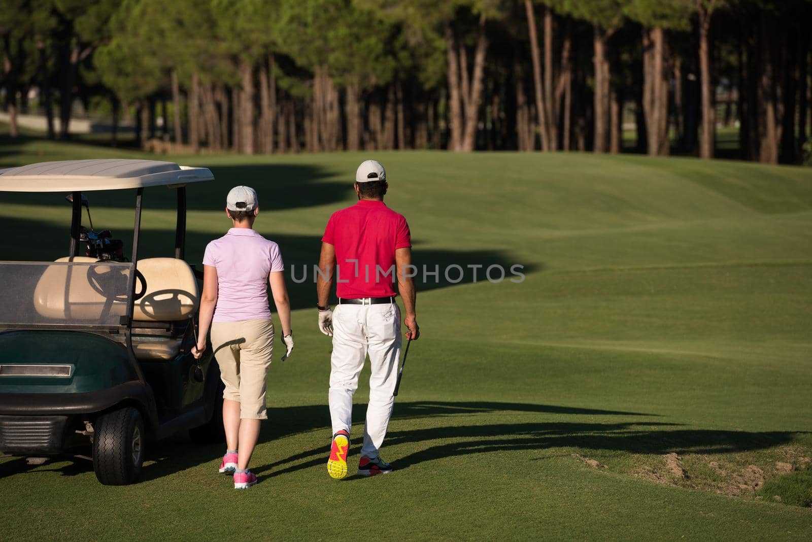 young couple walking to next hole on golf course. man carrying golf bag