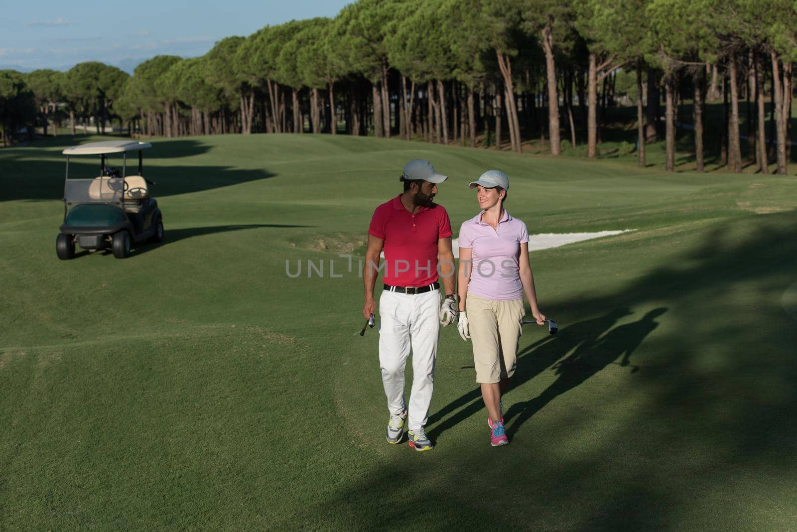 young couple walking to next hole on golf course. man carrying golf bag