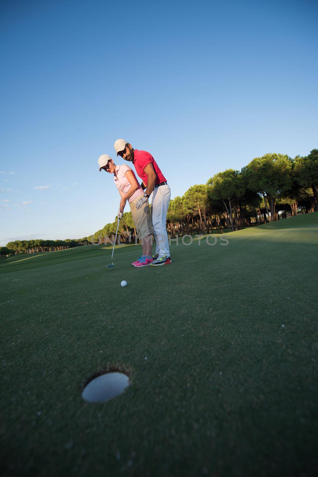 male golf instructor teaching female golf player, personal trainer giving lesson on golf course