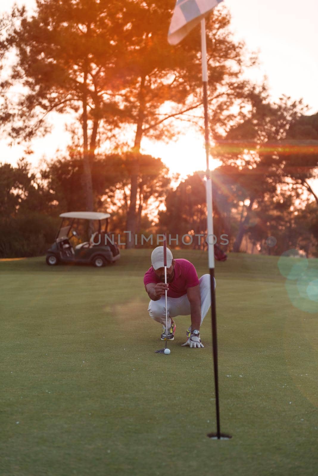 golf player aiming shot with club on course at beautiful sunset with sun flare in background